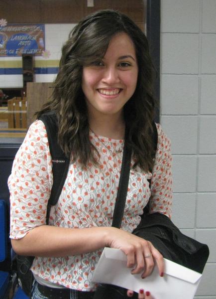 Brunette student recipient with award envelope wearing orange and white shirt with backpack