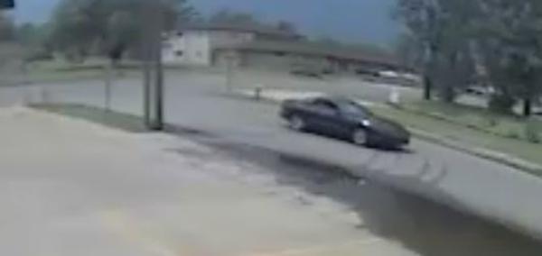 Dark colored 2-door vehicle driving down the street from street camera
