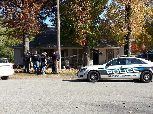Police of Baxter Springs vehicle and several officers standing in front of a house