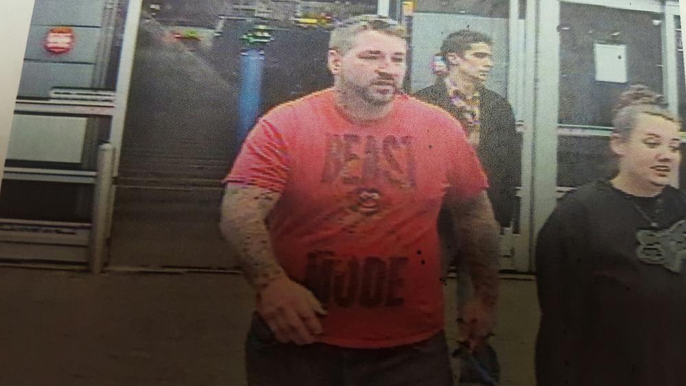 security camera image of a man and a woman leaving a store, the man wearing red Beast Mode shirt and woman wearing black Fox long-sleeved shirt