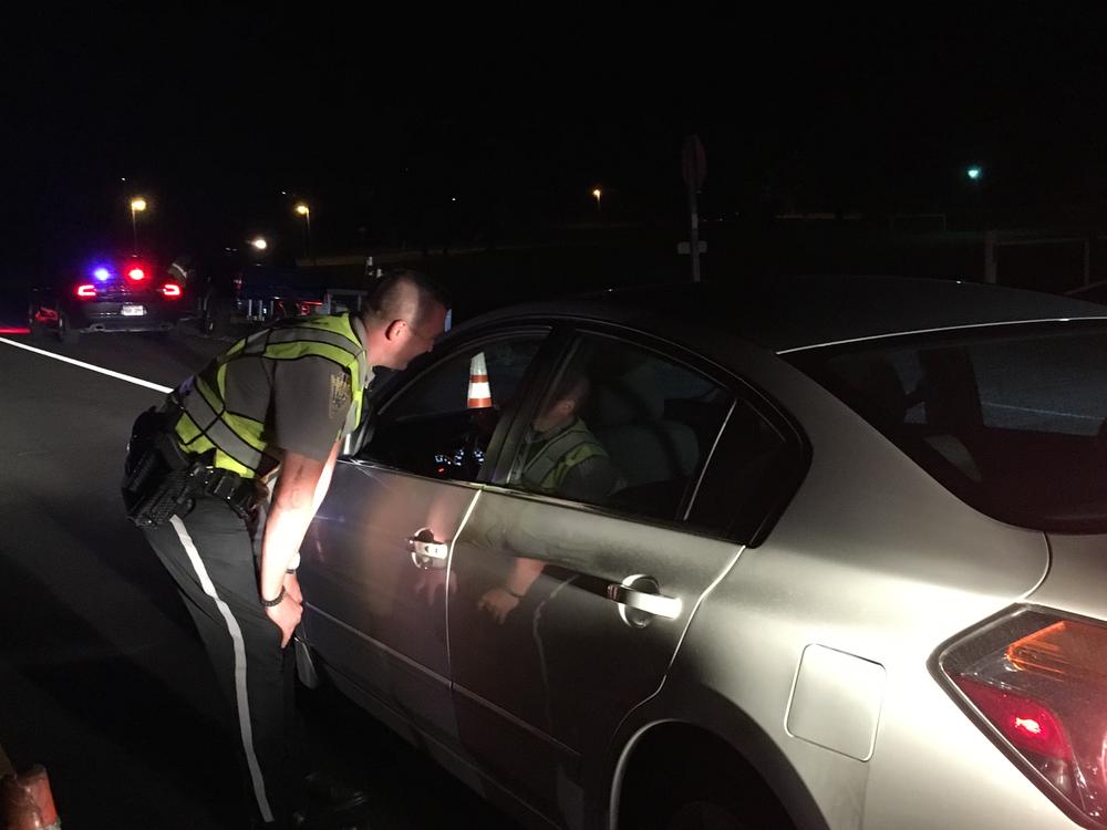 Officer leaning toward driver's open window at sobriety checkpoint